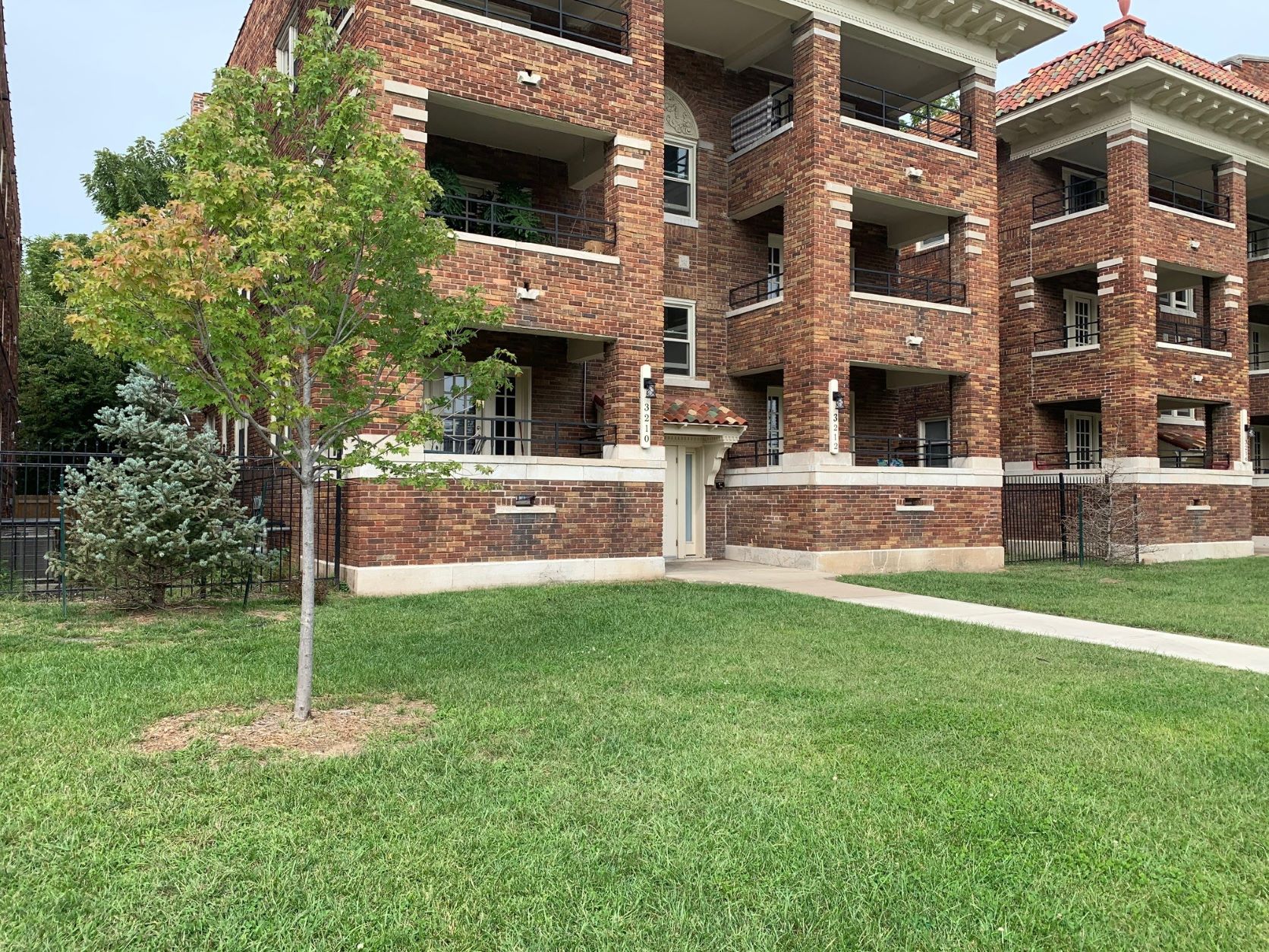 an apartment building with a lawn and a tree in front of it